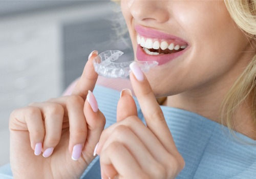 A woman holds up her Invisalign tray. Associates In Dentistry offers Invisalign in Elmwood IL.