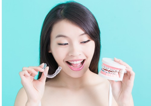 A young woman holds an Invisalign tray and a dental model. Associates In Dentistry offers Invisalign in Canton IL.