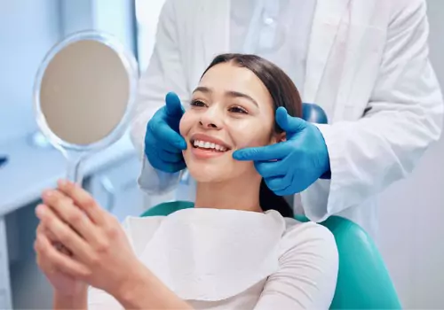 A woman smiling while looking at her teeth, after a teeth cleaning from a Dentist for Peoria IL