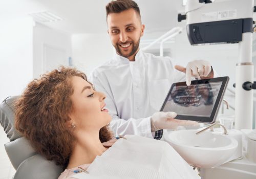 Dentist in Canton, IL showing a patient a dental crown treatment plan on a tablet in a modern dental office, Associates In Dentistry.