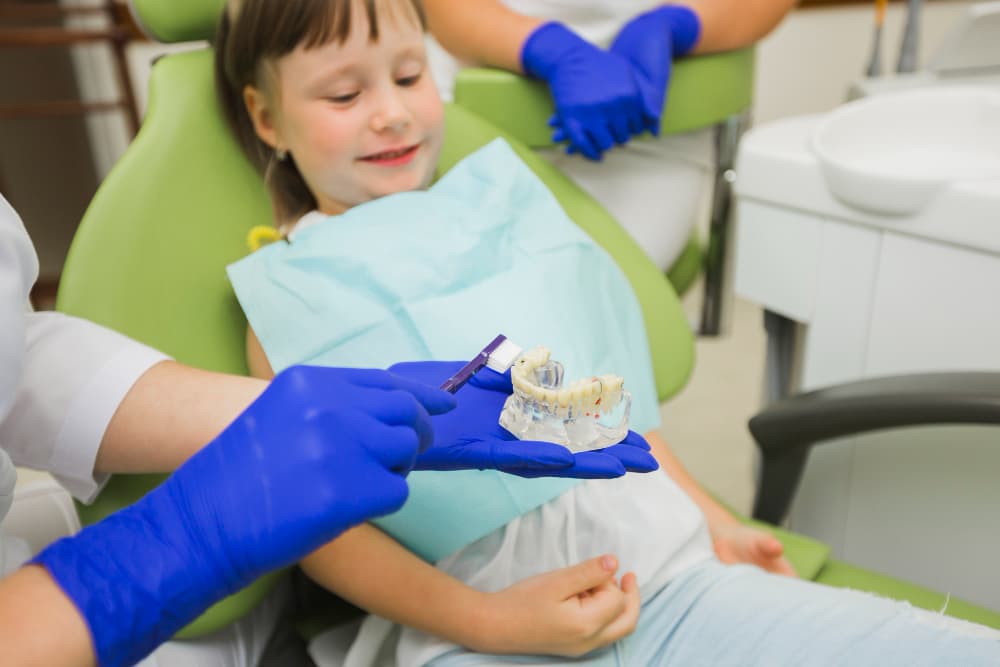 Child receiving pediatric dental care at Associates in Dentistry, Canton, IL, with hygienist and parent in a kid-friendly dental office.